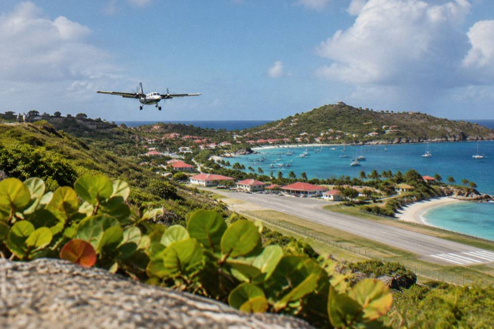 View from a hillside over a small airport terminal and a bay with turquoise water