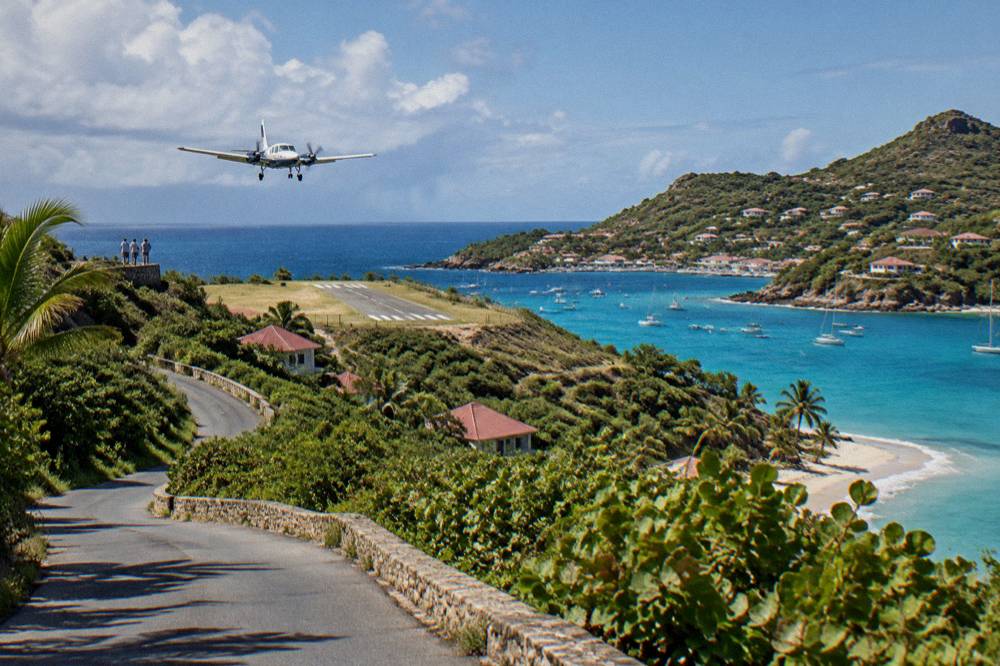 A narrow island road winding between green hills above a Caribbean bay