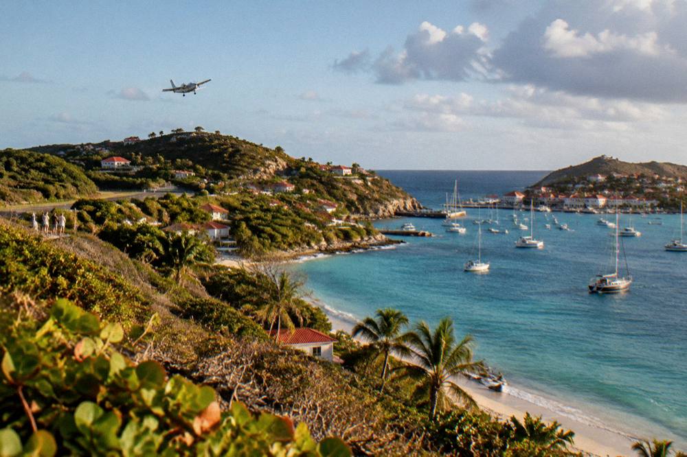 Sunlight over a calm Caribbean bay with a small airplane climbing away in the distance