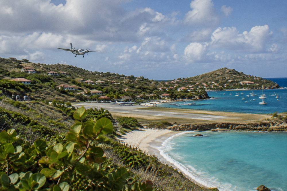 A curved sandy beach beside a runway with a few parked small aircraft