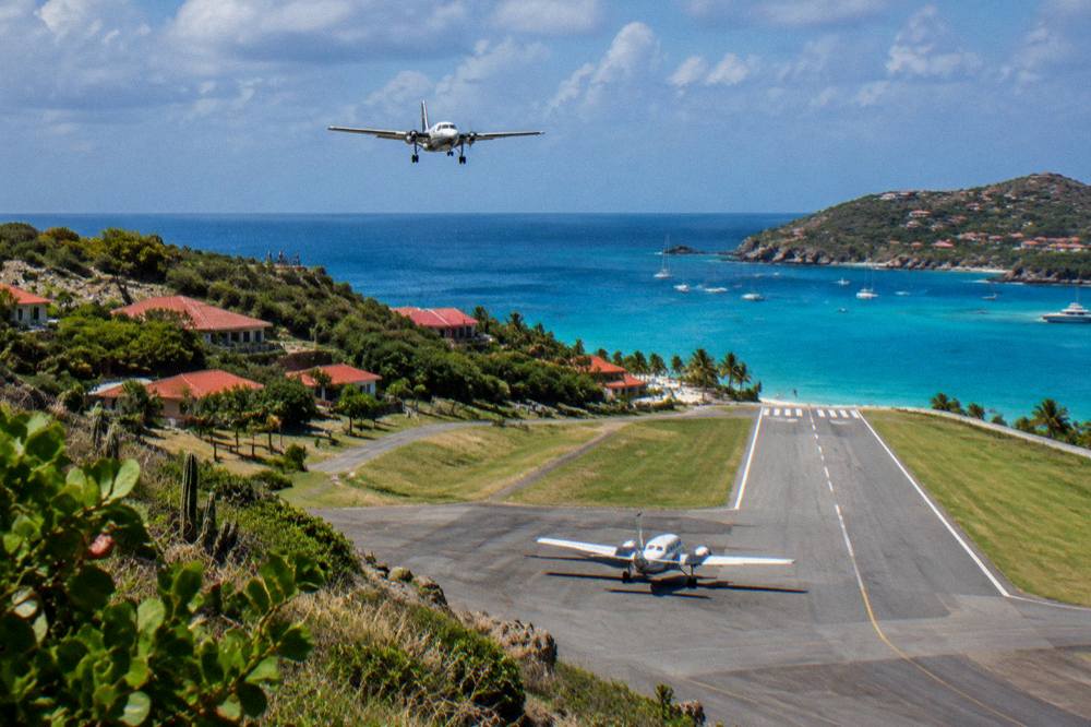 A small airplane taxiing on a short runway with palm trees and blue water at the far end