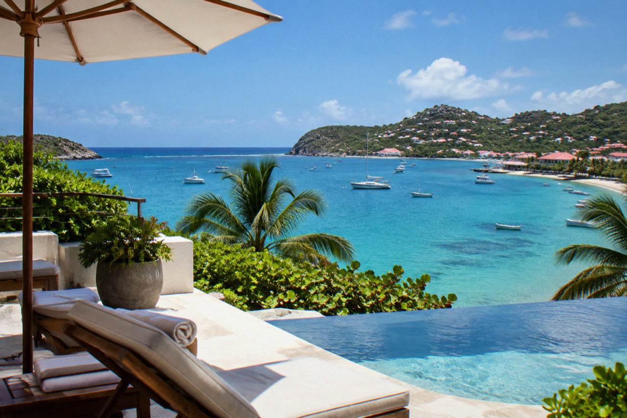 A modern hotel terrace overlooking a calm turquoise bay with hills in the distance