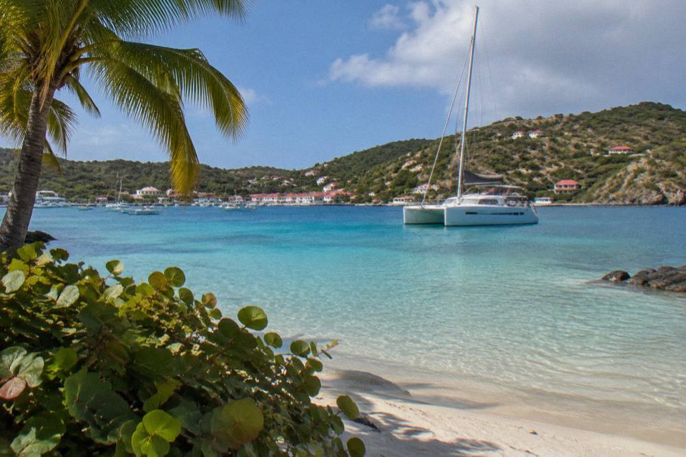 A white sailing catamaran anchored in a clear bay with wooded hills rising behind the shoreline