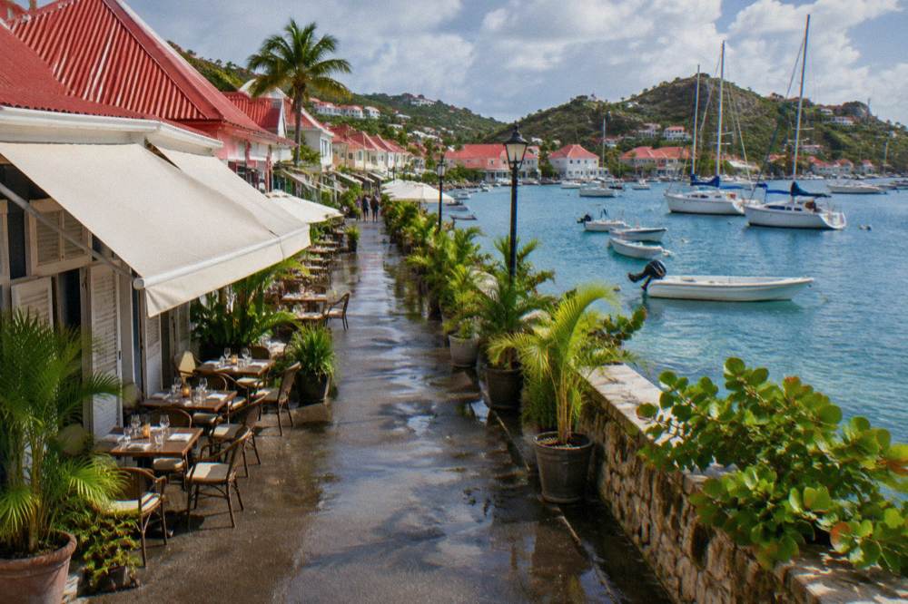 Tables set for dinner beside a harbour with boats at anchor in the evening light