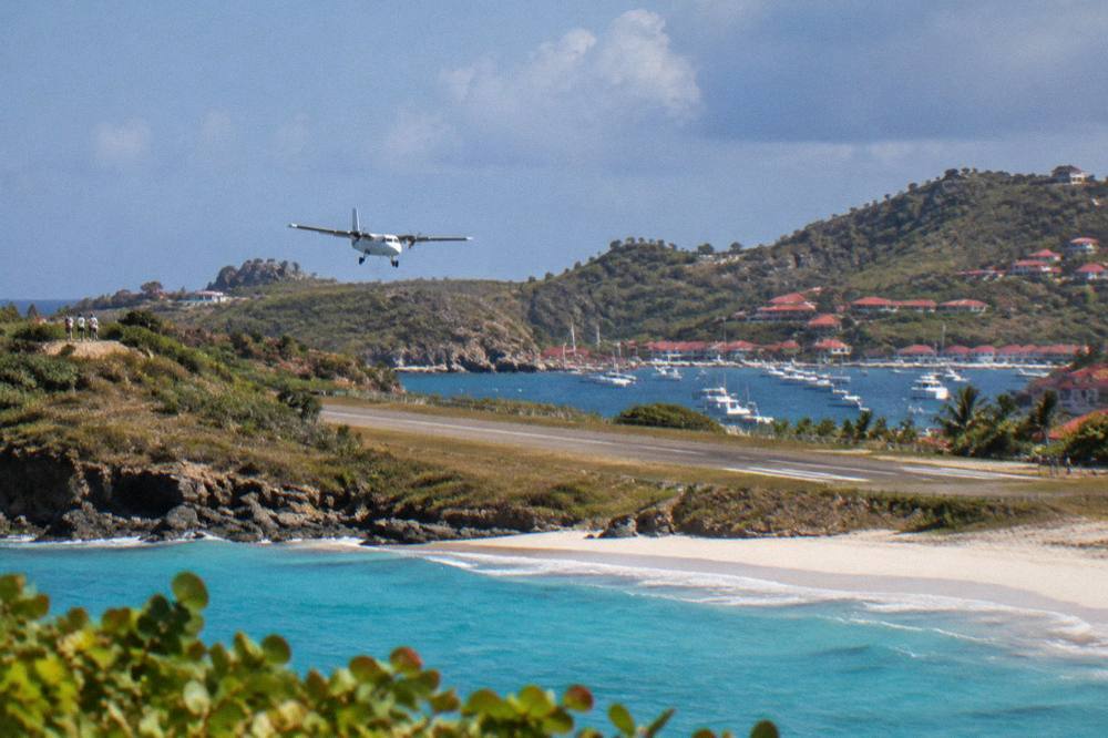 A small turboprop aircraft on a short runway beside a Caribbean beach