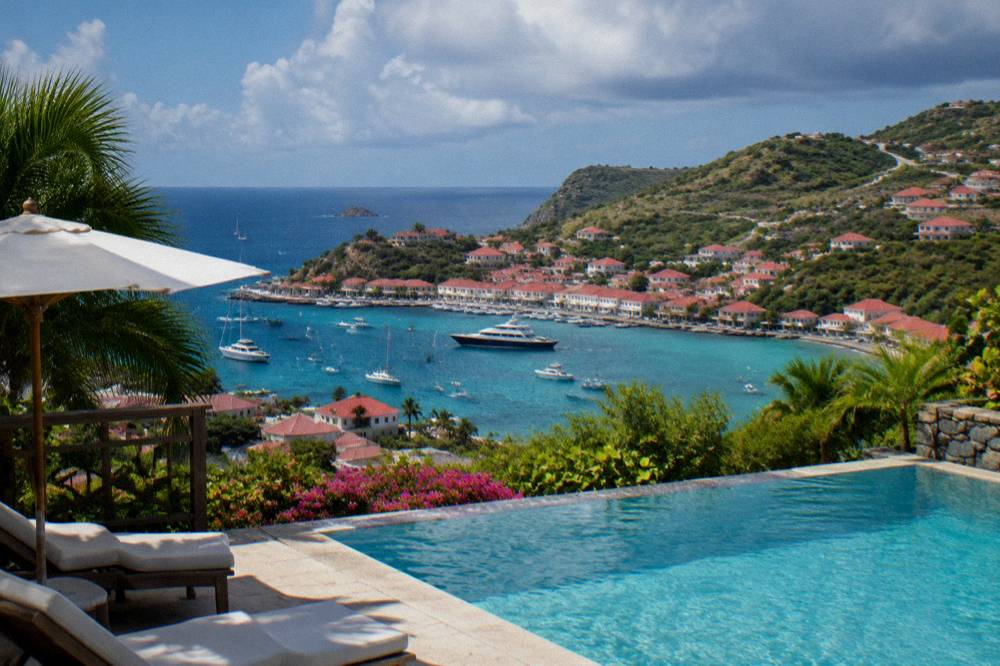 A hillside pool at midday with a wide view over green slopes to the sea