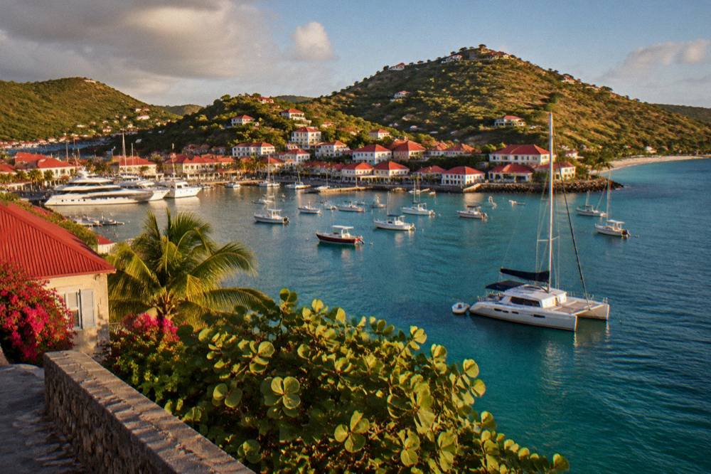 A sailing catamaran moored in a calm bay with green hills behind