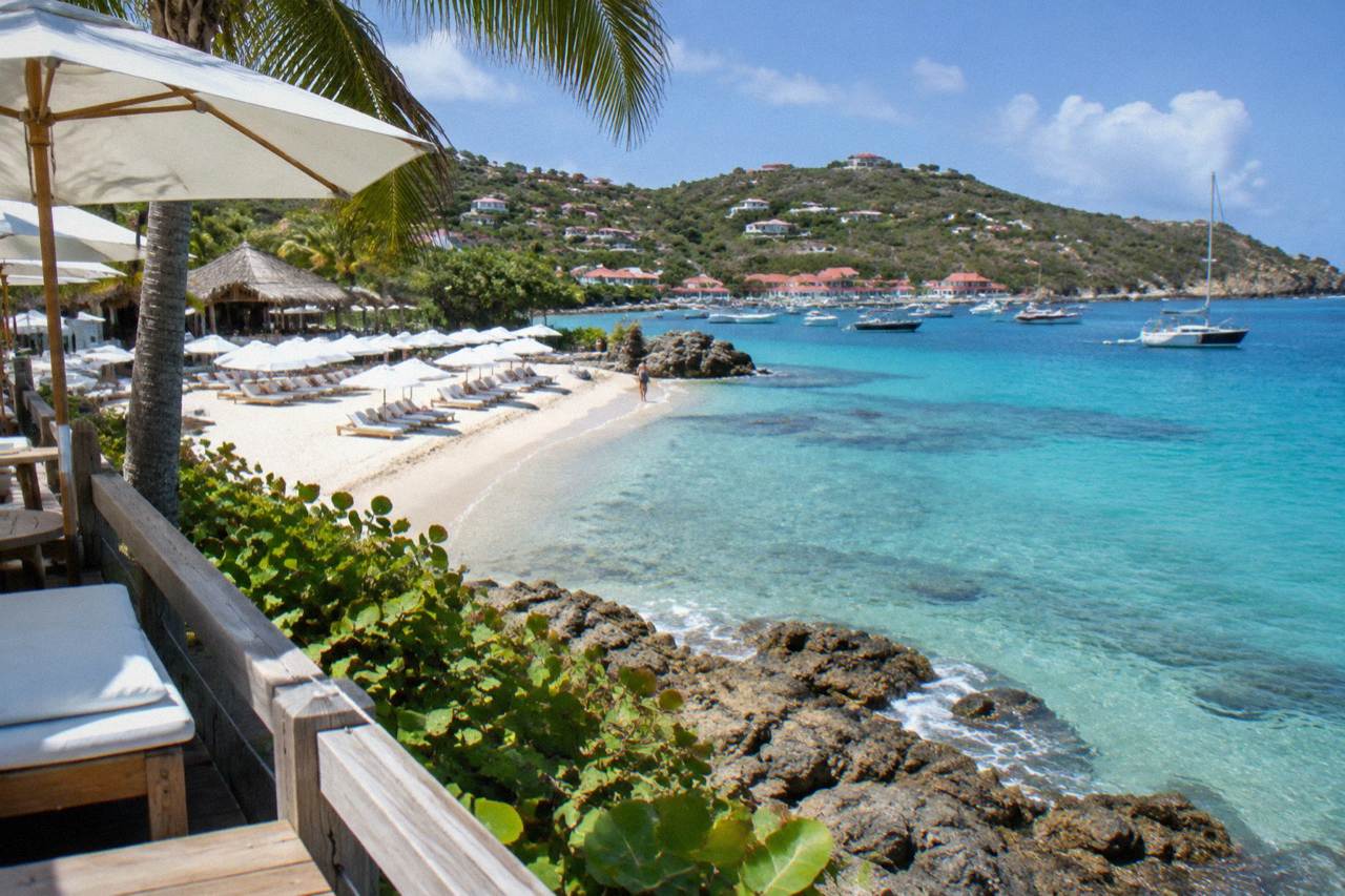 A beach club terrace above a rocky shoreline with turquoise Caribbean water and boats at anchor