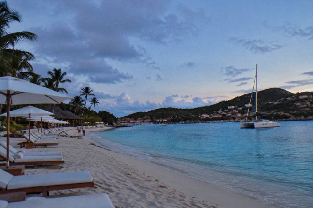 A sailing catamaran anchored in a quiet bay with green hills behind