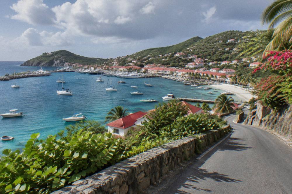Narrow winding road descending a green hillside toward the sea on St Barts