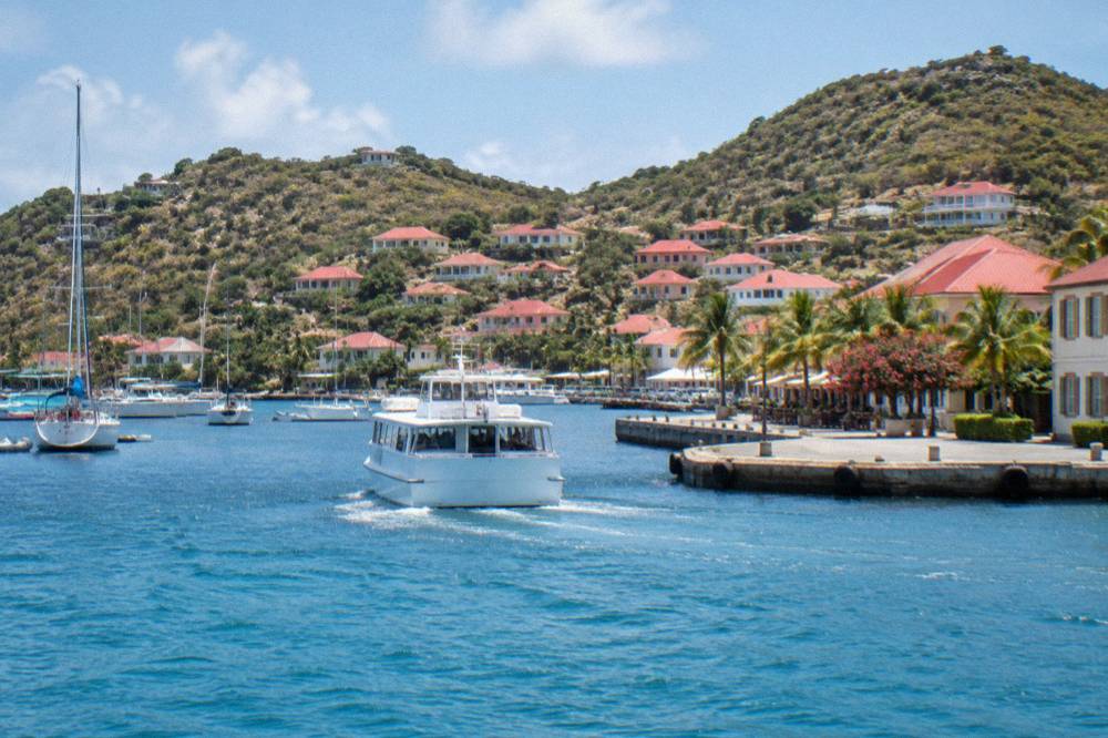 Small white ferry boat approaching a harbour quay with hills behind