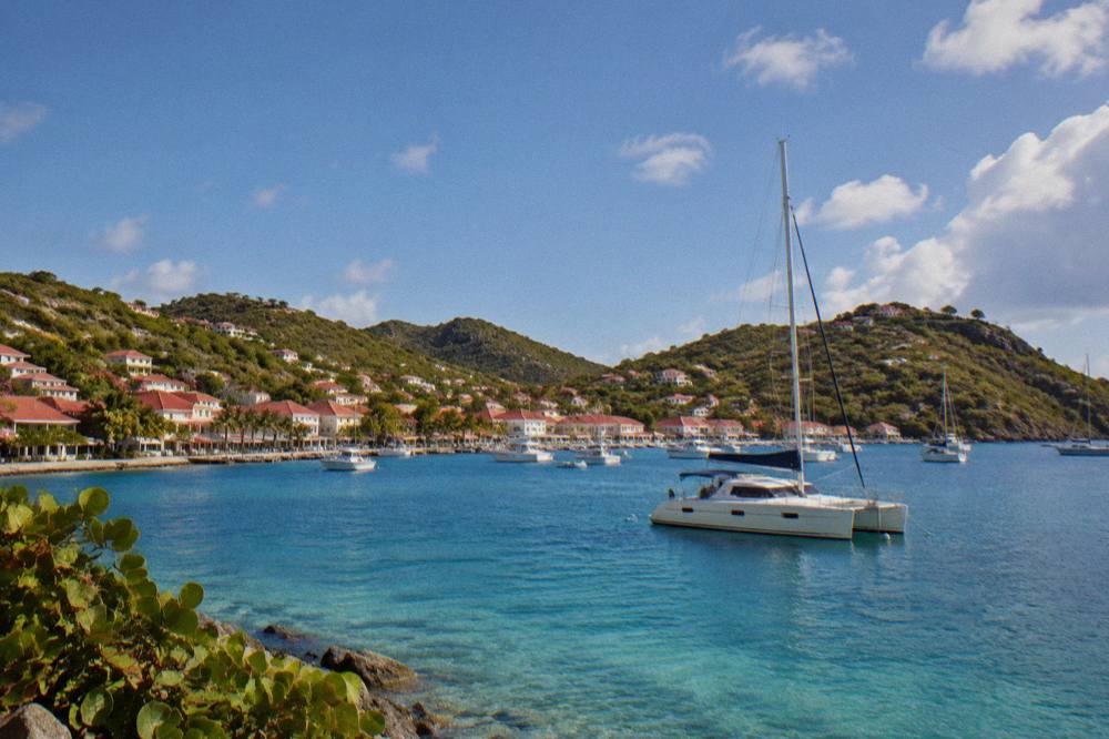 Sailing catamaran anchored in a quiet bay with clear water and green hills