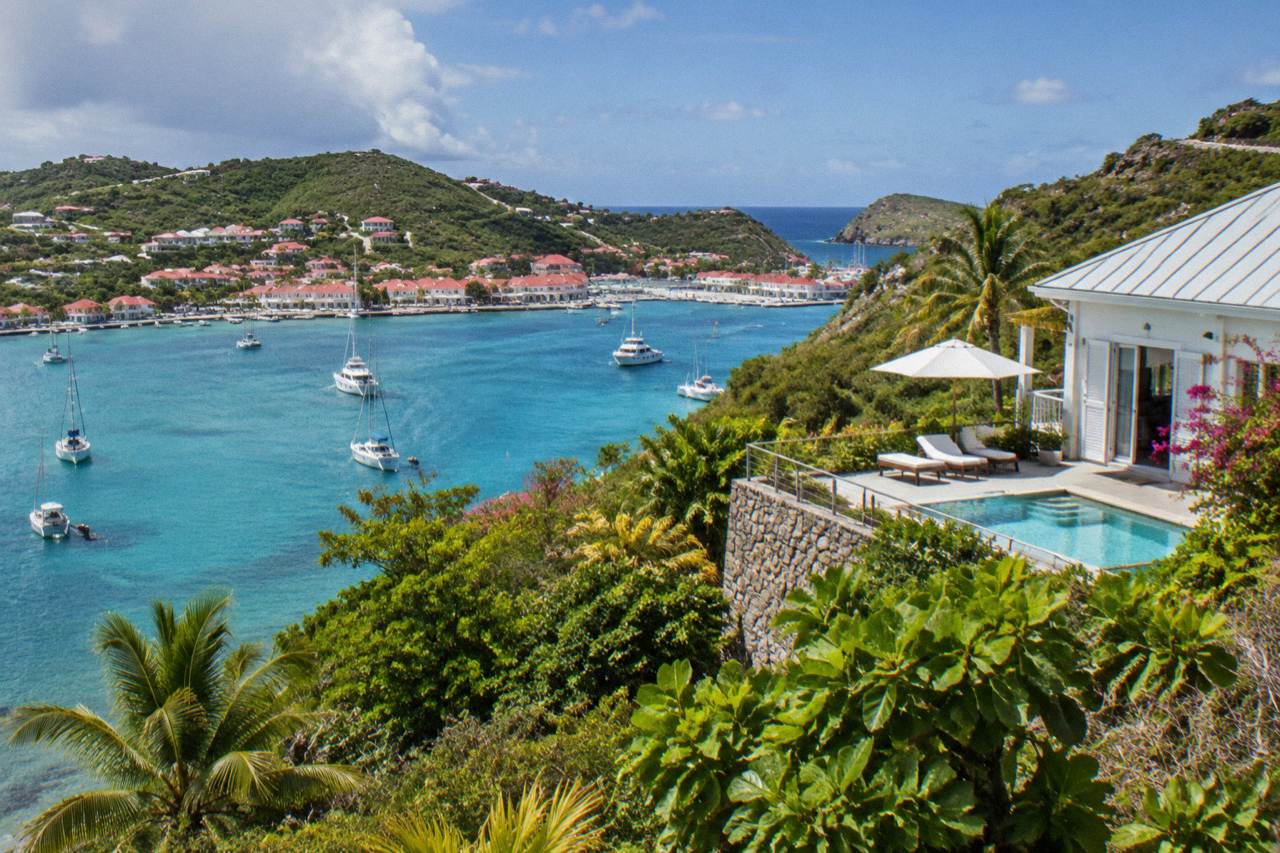 White vacation rental villa with a pool terrace above a turquoise bay on a green tropical hillside