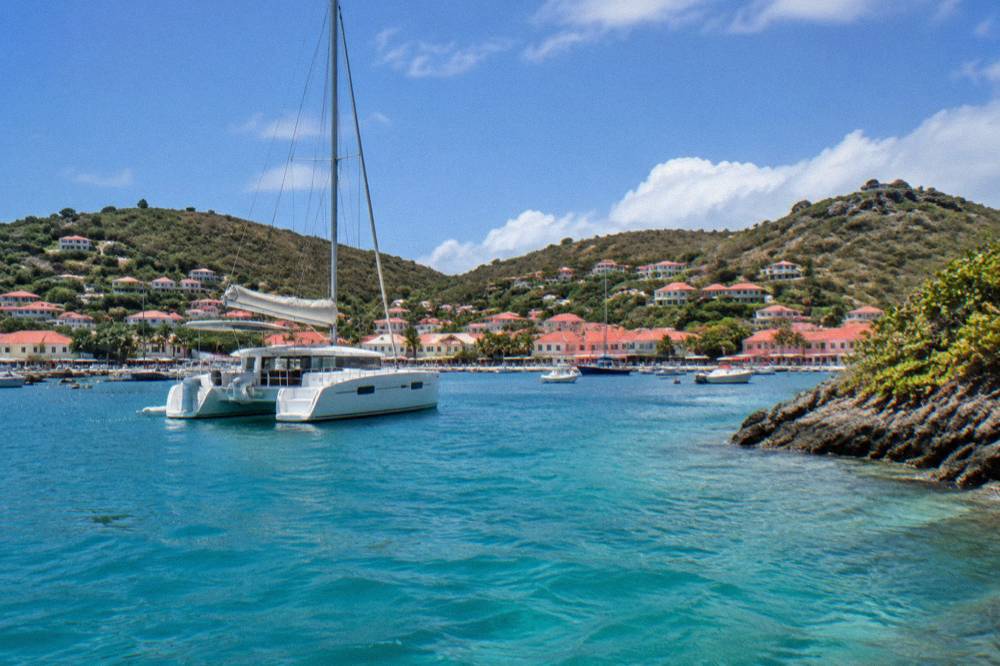Sailing catamaran anchored in clear water near a rocky green island shoreline