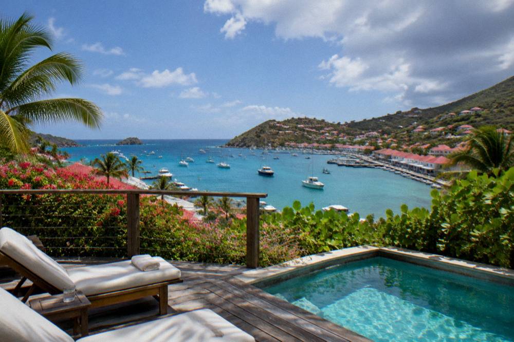Wooden terrace with loungers and a small plunge pool overlooking a bay with boats at anchor