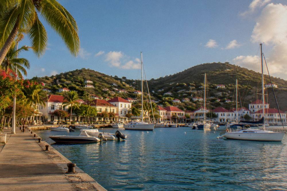 Harbor town with red roofs and masts of sailing boats along a quay in late afternoon light