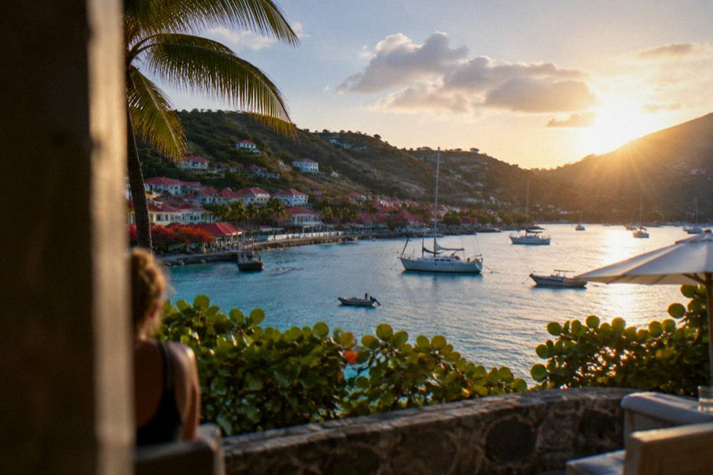 Sunset over a calm Caribbean bay with a few anchored boats and dark green hills