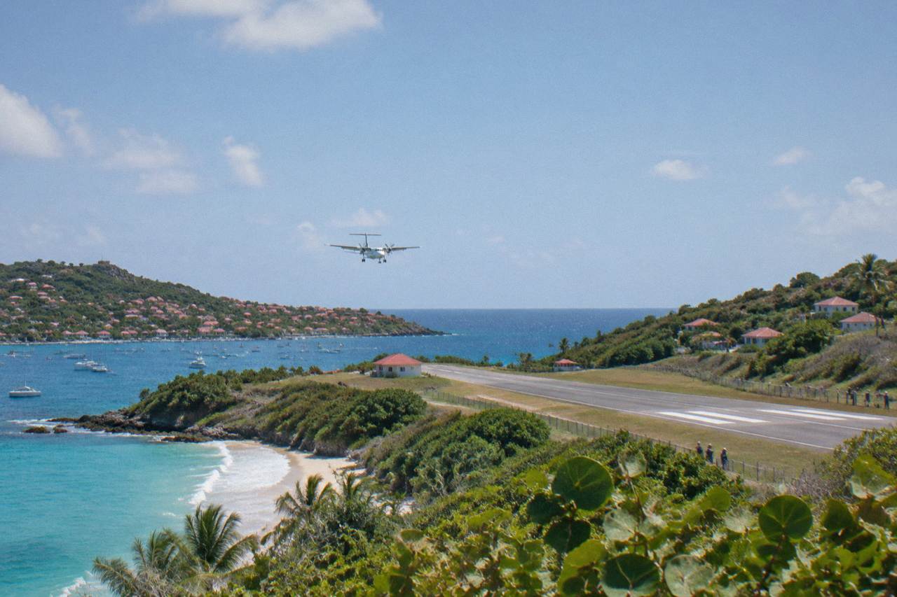 A small turboprop aircraft parked on a short runway between green hills and the Caribbean sea