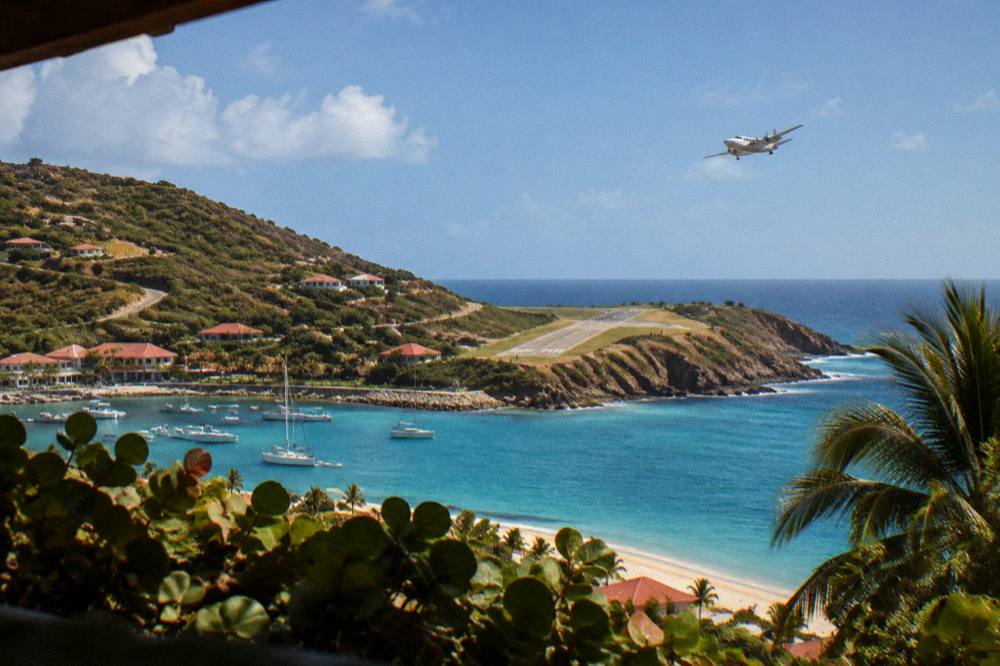 A small airplane climbing away from a runway toward a bright blue sky over the sea