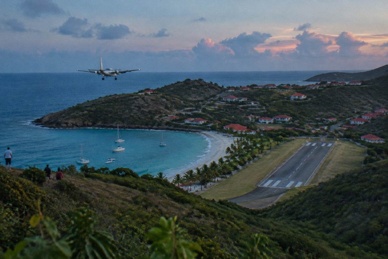 A small turboprop aircraft on a short runway between green hills and a Caribbean bay