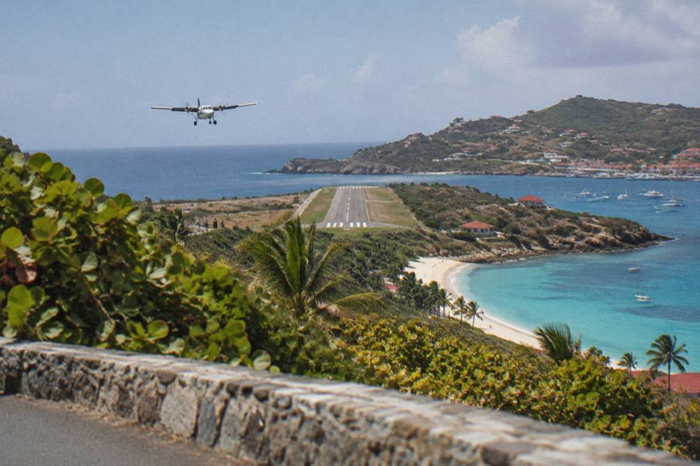 The end of a short runway seen from a hillside road above a Caribbean bay