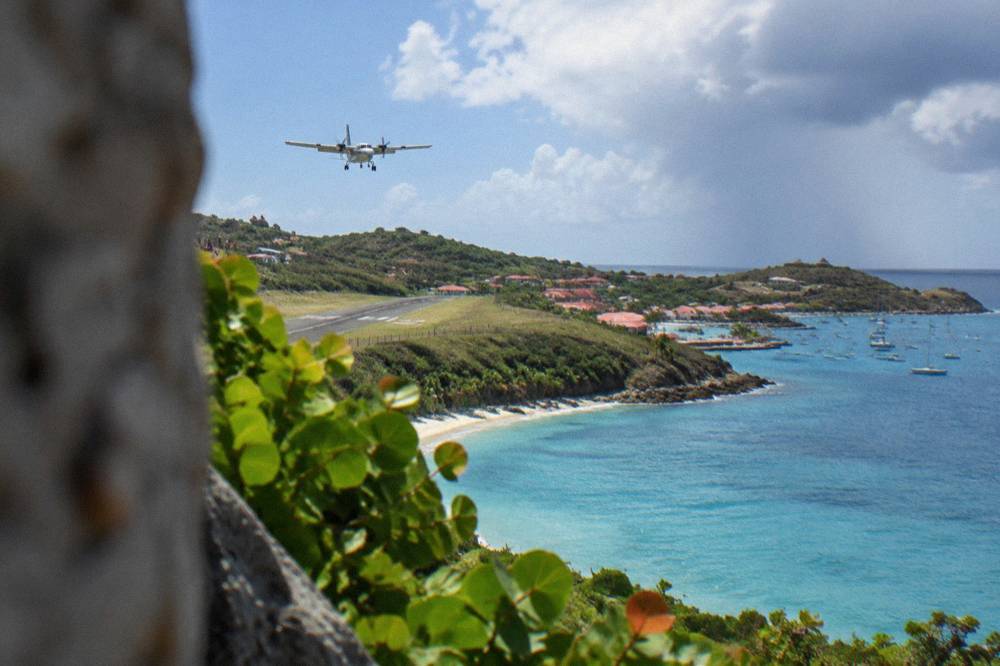 A twin-engine turboprop climbing away from a coastline over blue Caribbean water