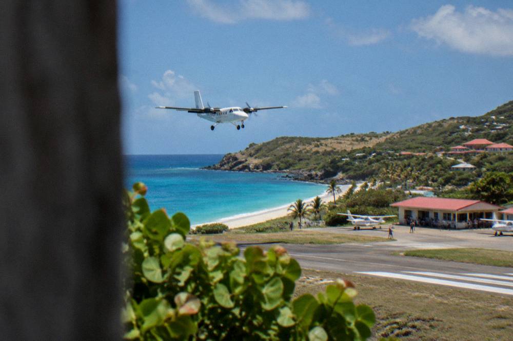 A small low airport terminal building with a few travelers standing beside parked light aircraft