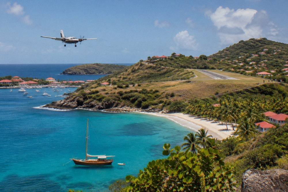 A wooden sailboat anchored in clear turquoise water beside a palm-lined Caribbean beach