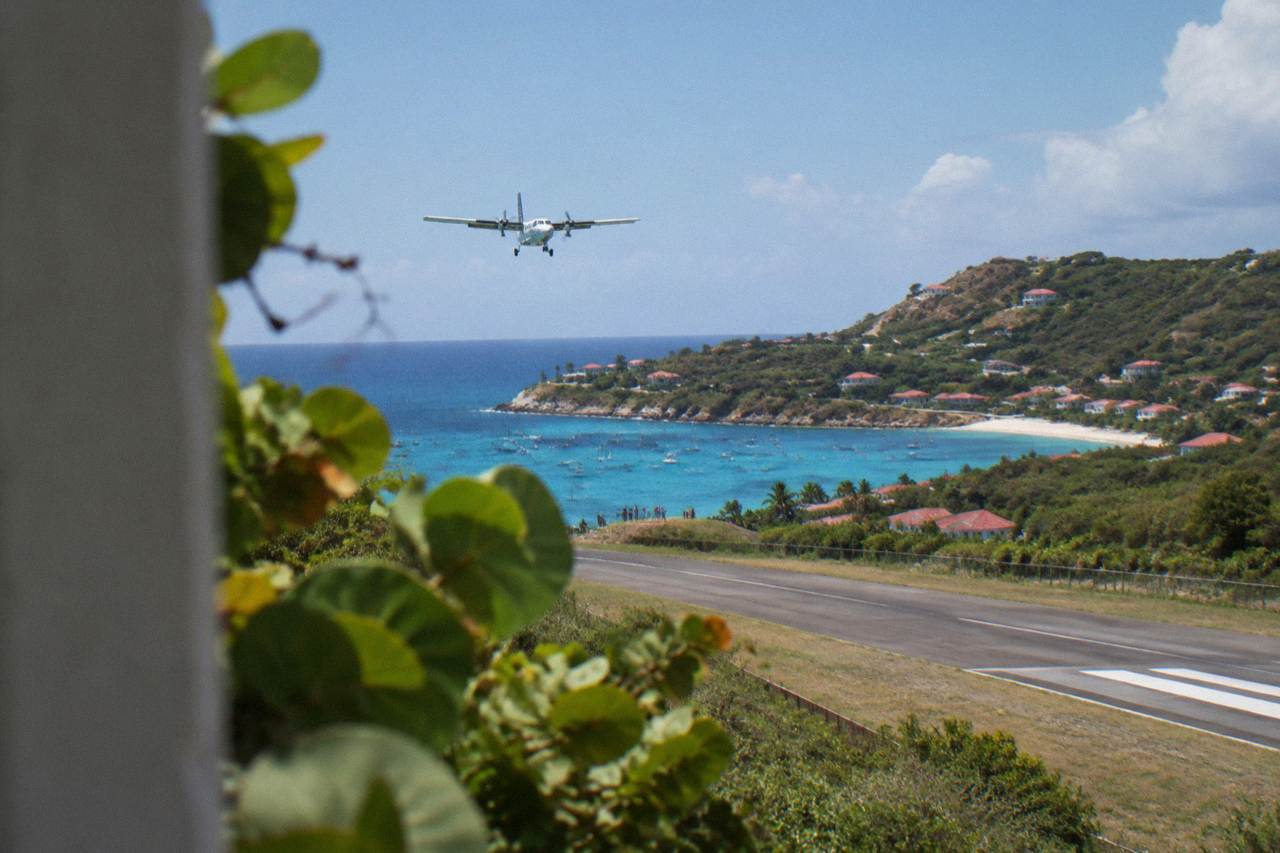 A small turboprop aircraft on a short runway between green hills and a Caribbean bay