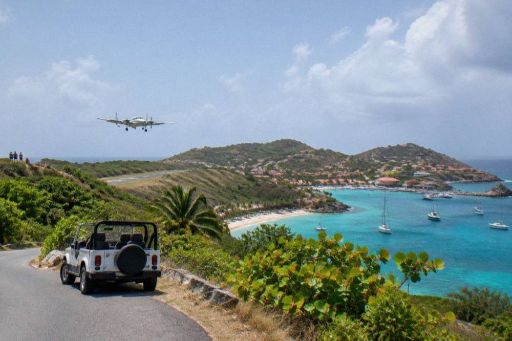 A small open-top rental car parked beside a narrow winding island road with sea views