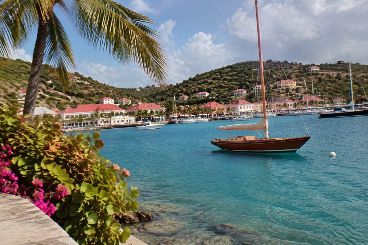 A wooden sailboat anchored in turquoise water off a green hillside on a Caribbean island
