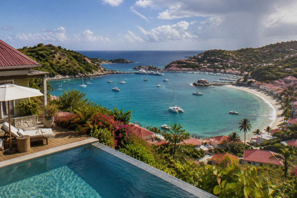 A hillside hotel terrace with a plunge pool overlooking a curved bay and turquoise sea
