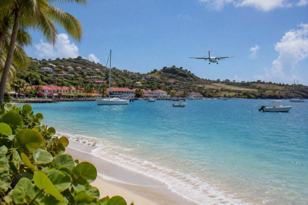 A small turboprop airplane descending over a hill toward a short runway beside a beach