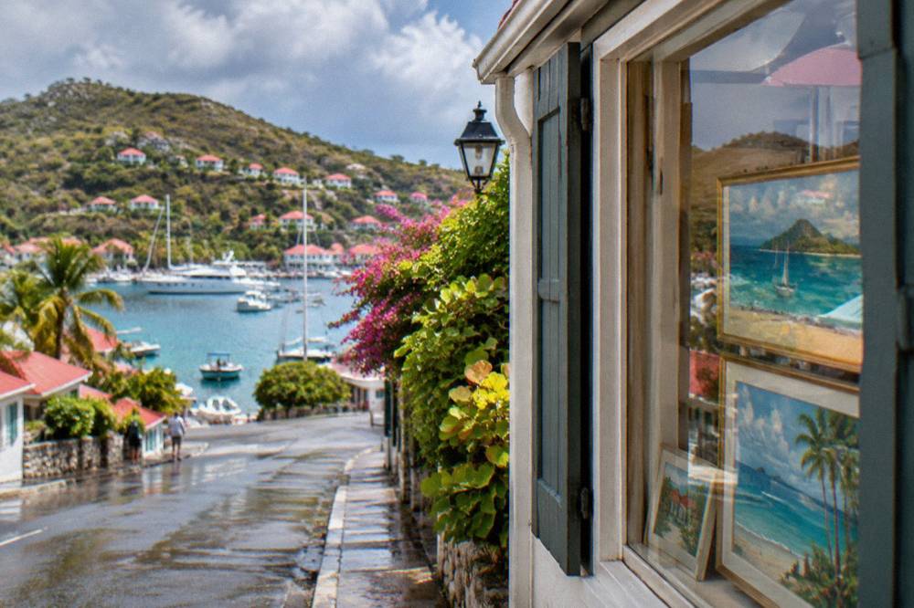 Paintings displayed in the window of a boutique on a narrow Gustavia street
