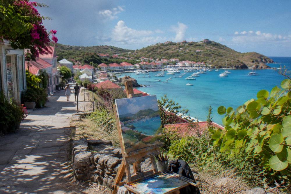 An artist's easel on a hillside overlooking a turquoise Caribbean bay