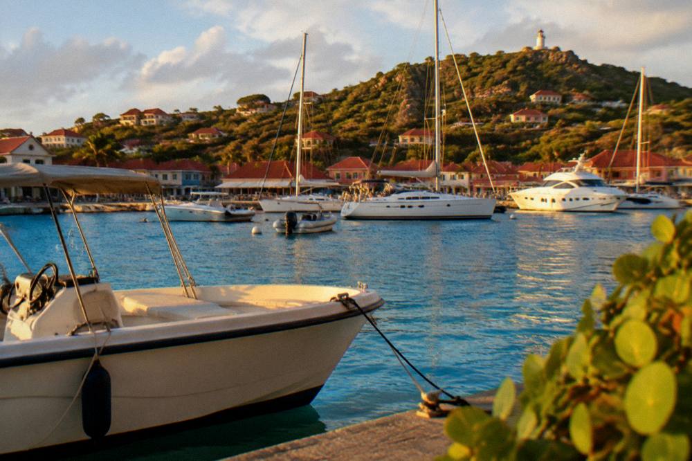 Yachts at anchor in Gustavia harbour beneath red-roofed buildings in late light