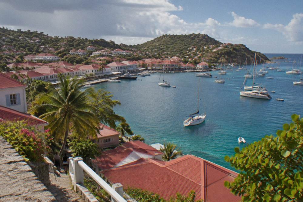 Sailing yachts and small boats moored in a harbour with white buildings on the shore