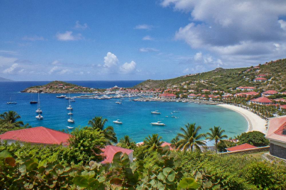 A hillside view over red rooftops, a harbor and a curved beach below