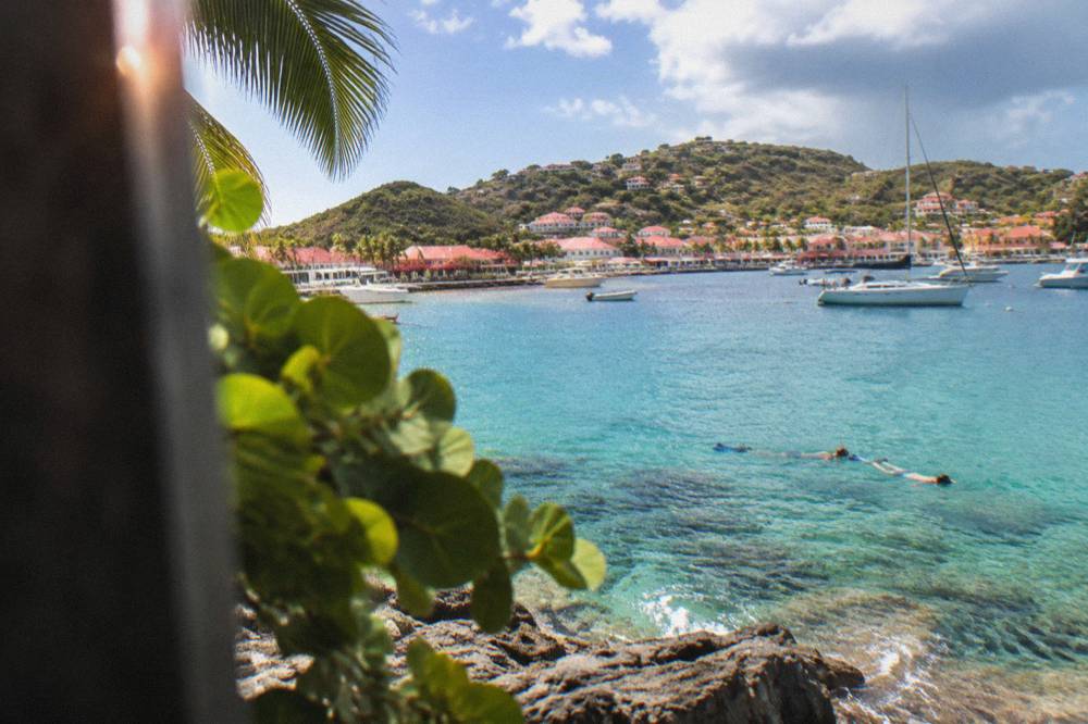 Snorkelers floating over clear water above rocks and coral near a St Barts headland