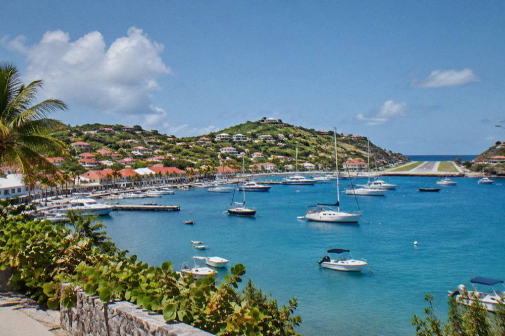 White buildings and palm trees above a curving bay with a runway ending at the water's edge