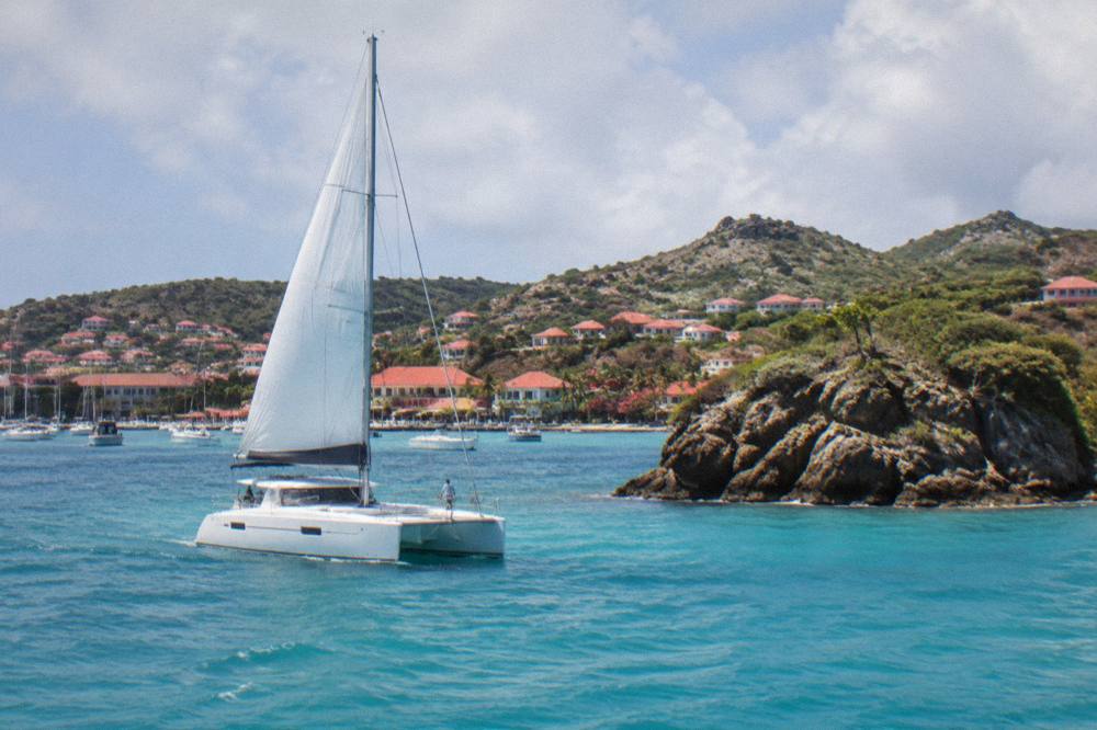 A sailing catamaran on turquoise water near a rocky Caribbean islet