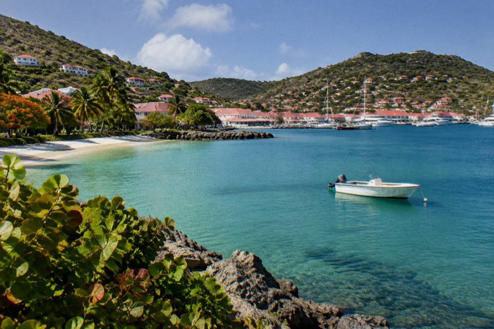 A small boat anchored in a quiet green bay with a white sand beach
