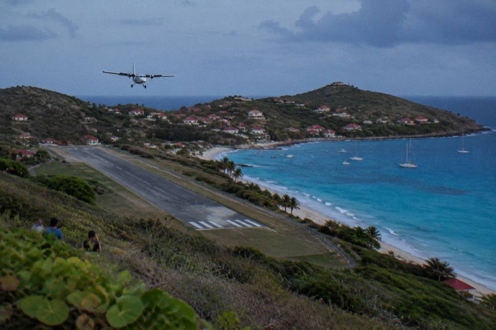 A small turboprop aircraft on a short runway beside a Caribbean beach