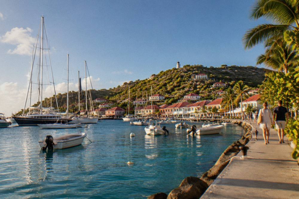 Tall masts of sailing superyachts moored in a harbor with a small town rising behind