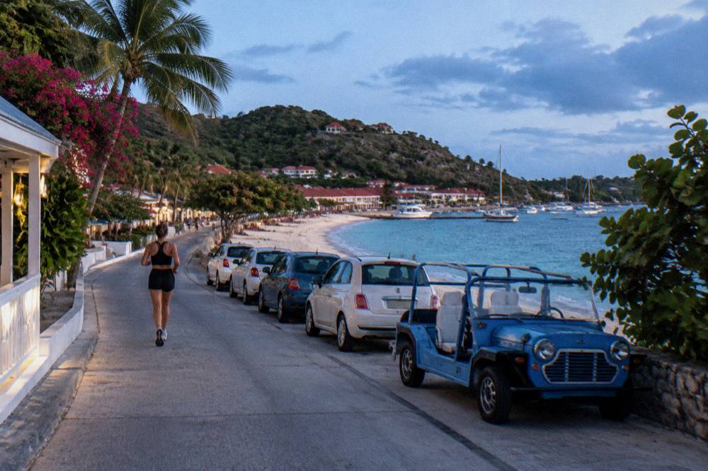 A row of small rental cars and a Mini Moke parked in the sun near a beach road