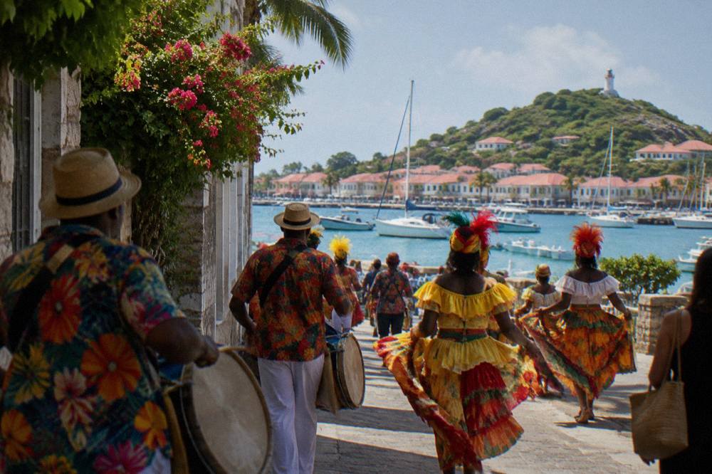 Drummers and costumed dancers moving through a narrow Caribbean street