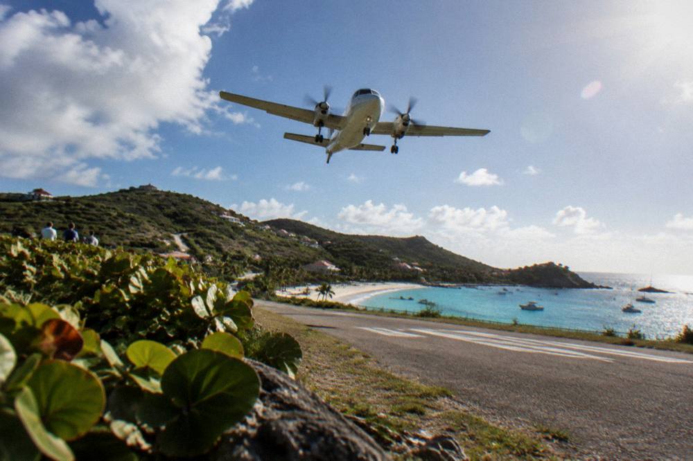 A small turboprop aircraft on a short runway between a beach and green hills
