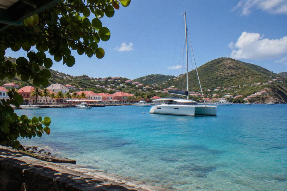 A sailing catamaran anchored in a quiet bay with green hills behind