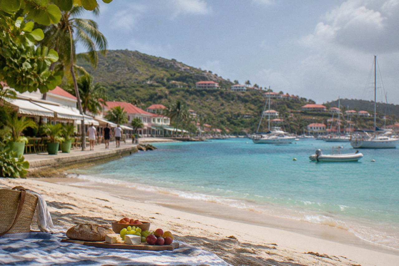 A simple picnic of bread, cheese and fruit on a beach towel beside turquoise water