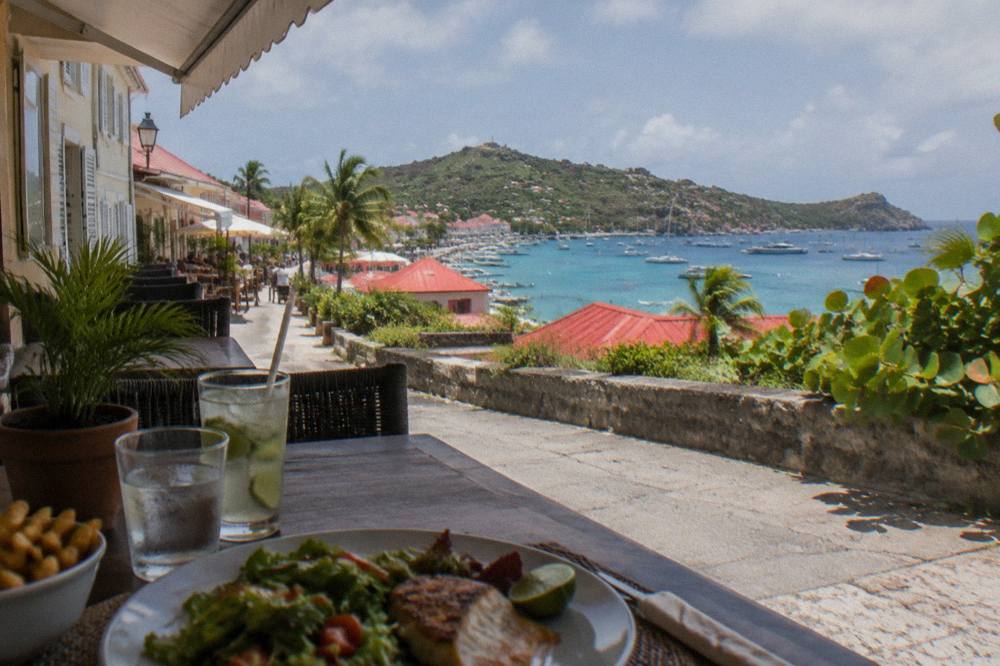 A shaded terrace table with a simple lunch and a view over rooftops to the sea